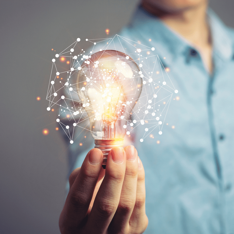 Main tenant une ampoule illuminée entourée de connexions numériques, symbolisant l’émergence d’idées et l’innovation technologique
