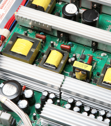 Gros plan sur une carte électronique équipée de transformateurs, condensateurs et radiateurs en aluminium, illustrant des composants de puissance