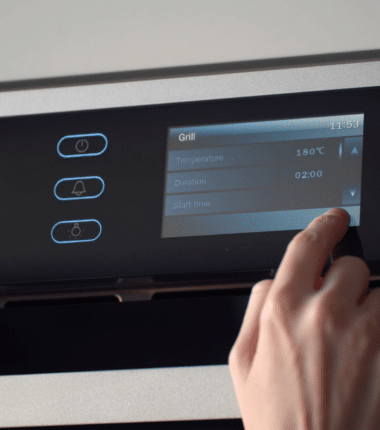 Main utilisant un écran tactile pour régler la température et les paramètres d’un four moderne