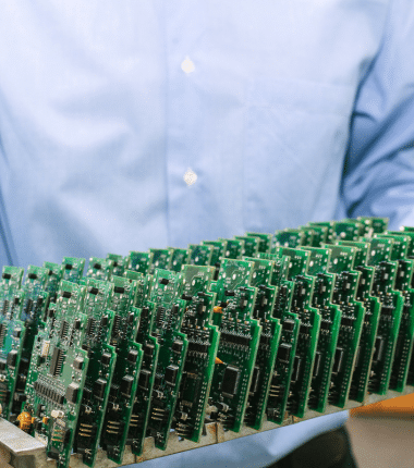Personne tenant un support rempli de nombreuses cartes électroniques vertes alignées en atelier de production