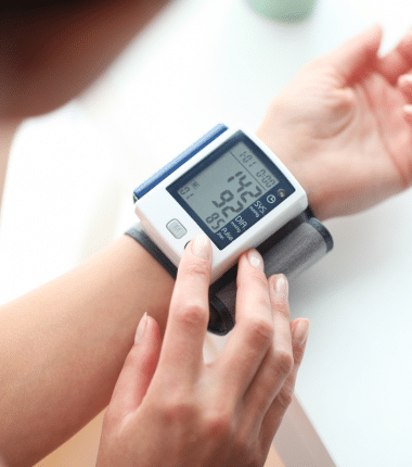 Personne utilisant un tensiomètre électronique au poignet pour mesurer sa tension artérielle, l’écran affichant les valeurs relevées