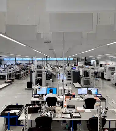 Technicienne en laboratoire industriel assemblant une carte électronique avec des outils de précision, portant des gants et des lunettes de protection